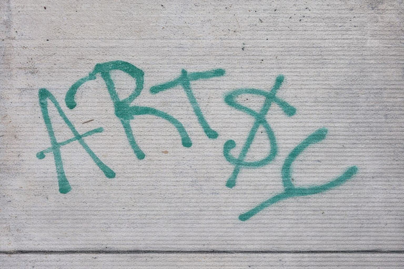 Grønn graffiti med teksten ART$ sprayet på en grå betongvegg.